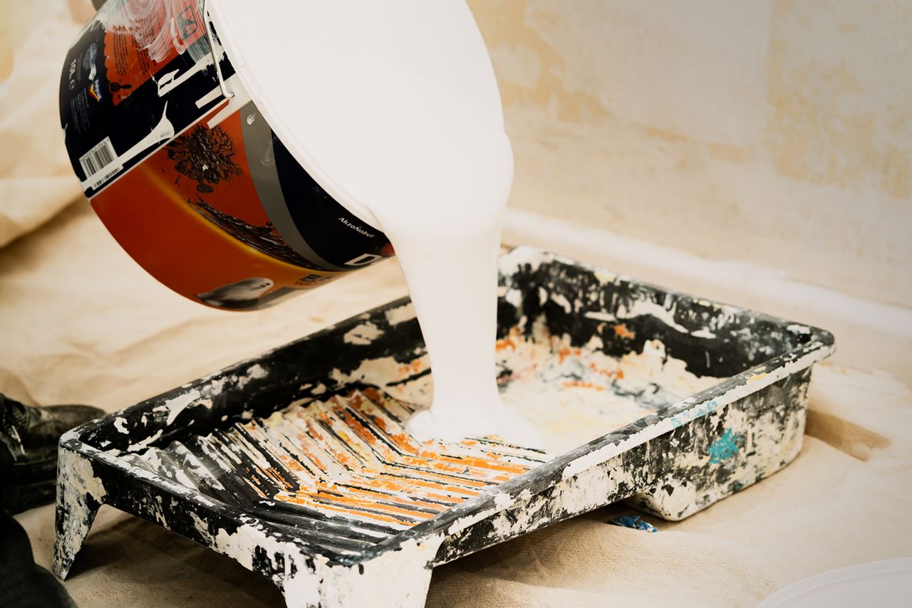 White paint being poured into a tray for home renovation, showcasing the preparation for a painting project.