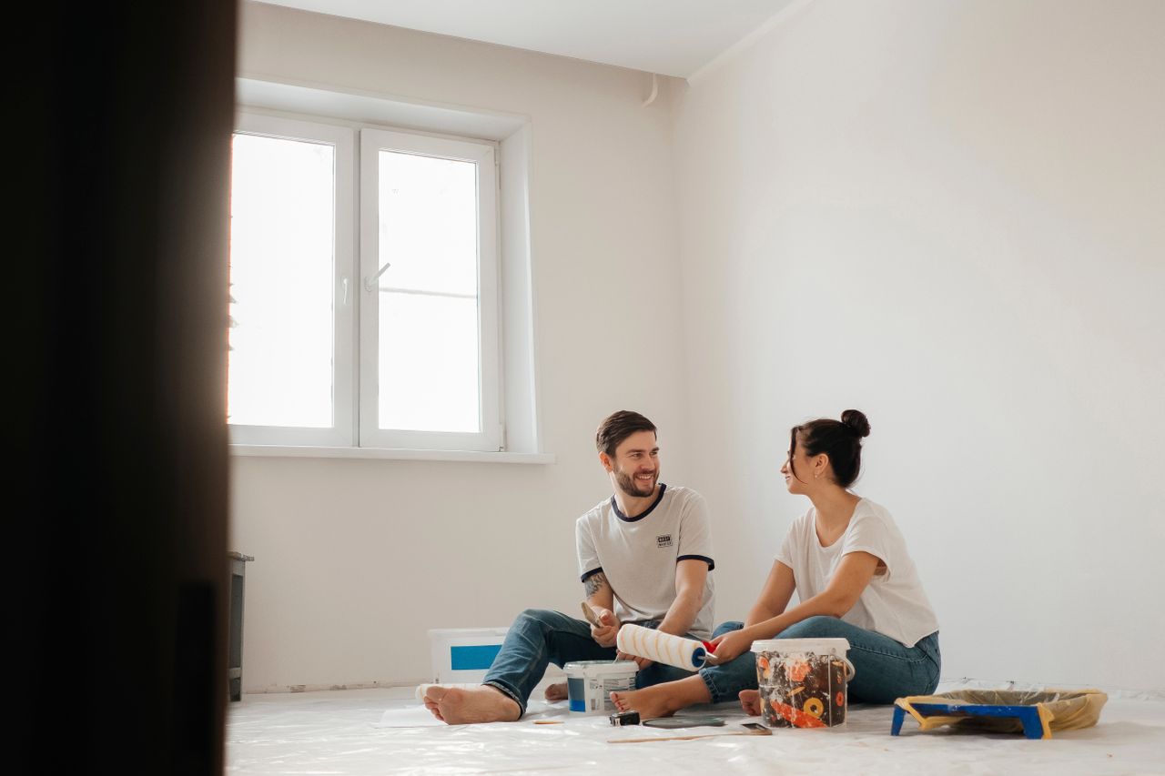 A joyful couple sitting on the floor, painting their new apartment and enjoying each other's company.