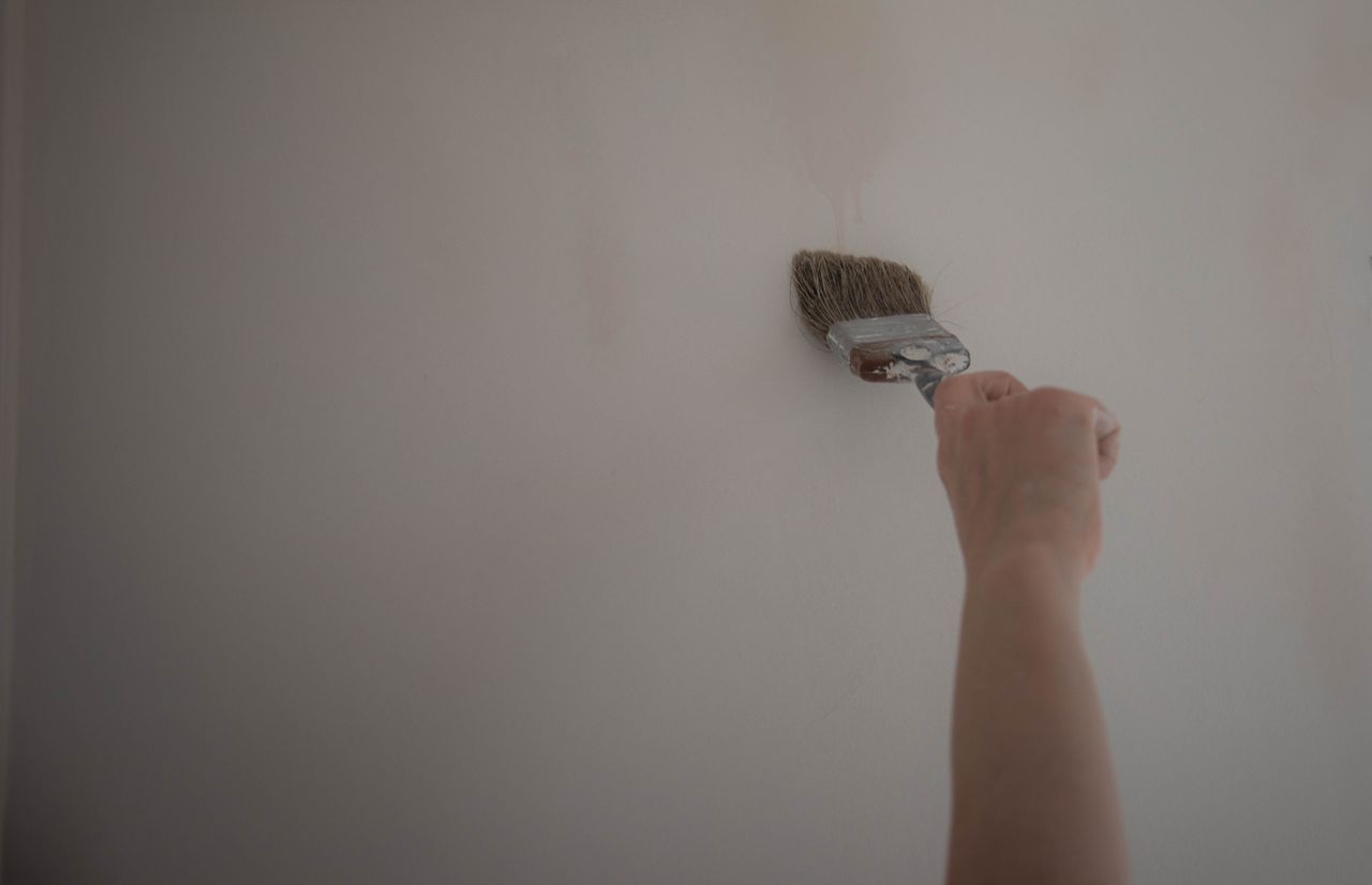 Hand using a paint brush to apply a coat of paint on a wall, highlighting DIY home improvement.